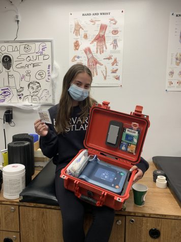 In the middle school trainer’s office in the Marshall Center, Sophia Levin ’25 holds an AED kit and supplies from a first aid kit.