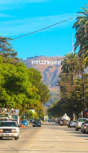 Hollywood sign district in Los Angeles, USA. Beautiful Hollywood highway road with cars, palms and a sign on the hills. Clear blue sky.